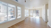 This well-designed single-floor unit offers a clean, contemporary aesthetic with an emphasis on natural light and functional layout. The open living and dining area is anchored by light-toned hardwood flooring and flanked by large windows dressed with horizontal blinds, flooding the space with abundant daylight. A sliding glass door provides direct access to an outdoor balcony, offering views of the surrounding urban environment.

The kitchen is efficiently laid out in a galley style, featuring rich dark wood cabinetry with brushed metal hardware, white quartz countertops, and a classic subway tile backsplash. Stainless steel appliances, including a refrigerator, microwave, and range, complete the modern and functional cooking space.

The bedrooms are carpeted in a neutral tone and each benefit from generous window arrangements that bring in natural light while maintaining a calm, restful atmosphere. The rooms offer ample wall space suitable for a variety of furniture configurations.

The bathroom is well-appointed with warm wood vanity cabinetry, a white countertop with an undermount sink, a large mirror with modern lighting, and a walk-in glass-enclosed shower with tile surround. Light hardwood-style flooring ties the bathroom's design to the rest of the unit. Overall, the space presents a cohesive, modern design with bright, neutral tones throughout.