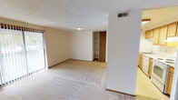 This single-floor residence offers a practical and comfortable layout designed for everyday living. The spacious living room is a central highlight, featuring wall-to-wall carpeting, a sliding glass door that fills the space with natural light and provides outdoor access, and vertical blinds for privacy. A built-in shelving unit adds functional storage to the living area.

The kitchen is efficiently arranged with warm wood-toned cabinetry extending to the upper and lower walls, a stainless steel sink, a dishwasher, an electric range with oven, and light-colored countertops. Tile flooring and overhead fluorescent lighting give the kitchen a clean, practical finish.

The bedrooms are carpeted and well-proportioned, each featuring sliding or hinged closets with built-in hanging rods and shelving. Windows in each bedroom allow for ample natural light, contributing to a bright and airy atmosphere. Textured popcorn ceilings are present throughout the unit, along with consistent wood-trimmed door frames that tie the interior together.

The full bathroom includes a tub-shower combination, a medicine cabinet with mirror, a single-sink vanity with wood cabinetry, and tile flooring. The neutral color palette and clean finishes throughout the space create a cohesive and move-in ready environment.