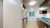Located in Portland, Oregon, this two-bedroom, one-bathroom unit offers a practical and well-organized single-floor layout. The living room is bright and open, featuring wood-style plank flooring, a textured ceiling, and a full-width sliding glass door that opens to lush green surroundings, filling the space with natural light and outdoor views. A hallway connects the living area to the rest of the unit, maintaining a logical and efficient flow throughout.

The galley-style kitchen is a visual standout, featuring striking teal laminate countertops that contrast boldly against dark espresso cabinetry. Stainless steel appliances, including an electric range with overhead ventilation, are complemented by ample upper and lower cabinet storage. A window at the end of the kitchen brings in additional natural light with garden views.

Both bedrooms are carpeted and offer a calm, neutral palette with white walls and sliding panel closets for storage. The primary bedroom is a comfortable size, while the second bedroom features a window with neighborhood views and a baseboard heater. The full bathroom includes a dark wood vanity with a single sink, a mirror, a shower/tub combination, and wood-look tile flooring, completing this functional and well-appointed home.