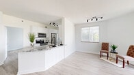 Located in Doral, FL, this single-story, 4-bedroom, 2-bathroom home offers a clean, modern aesthetic defined by a bright, neutral palette and light wood-style flooring that flows seamlessly throughout. The open-concept kitchen and living area serves as the heart of the home, where a sleek peninsula with granite countertops provides both workspace and casual seating. The kitchen is fully equipped with stainless steel appliances, white cabinetry, tile backsplash, and track lighting overhead. The adjoining living area benefits from large windows with horizontal blinds and a full-height sliding glass door dressed in vertical shades, filling the space with abundant natural light. Four well-proportioned bedrooms each feature windows with outdoor views, clean white walls, and the same light flooring found throughout. The primary bedroom offers a comfortable footprint with direct access to a dedicated closet. Both bathrooms are finished with granite-topped white vanities, large framed mirrors, and matte black fixtures. One bathroom includes a glass-enclosed walk-in shower with tile surround, while the second features a full soaking tub. Two hallways connect the layout efficiently, completing a thoughtfully organized and move-in-ready home.