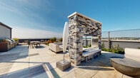 Located atop 42 Broad St W in Mount Vernon, NY, this rooftop terrace is a thoughtfully designed outdoor amenity space offering a rich combination of relaxation zones, landscaping, and striking open-air views. The terrace is finished with a mix of large-format stone pavers and warm wood decking that together create distinct zones across the expansive rooftop level.

A centerpiece pergola with a slatted overhead canopy provides shaded seating and defines the primary gathering area, which is furnished with lounge chairs ideal for outdoor leisure. Adjacent to this is a dramatic stacked-stone fireplace feature, built with natural ledger stone and fitted with a sleek stainless steel firebox, surrounded by additional seating and a low-profile sofa arrangement.

A dedicated green lawn area, lined with ornamental grasses and bordered by cedar planter boxes, offers a softer, more serene retreat and opens to unobstructed panoramic views of the surrounding cityscape and distant skyline. Landscaped plant beds run along the perimeter walls, adding texture and color throughout.

The terrace benefits from abundant natural light and open sky exposure, while its elevated position affords sweeping views in multiple directions. The overall design balances modern urban aesthetics with comfortable outdoor living, making it a versatile rooftop destination for both relaxation and entertaining.