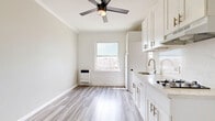 Located on the third floor of a building on Melrose Avenue in Los Angeles, this one-bedroom, one-bathroom unit offers a clean, minimalist aesthetic throughout. Light-toned luxury vinyl plank flooring runs continuously across the space, lending a cohesive and modern feel. The main living and kitchen area features exposed white-painted brick walls, adding a subtle industrial character, while a large window invites generous natural light and frames views of the surrounding Los Angeles neighborhood. White upper cabinetry and a full-size refrigerator define the kitchen corner, keeping the layout functional and efficient. A dedicated entry area provides a clear transition into the unit, with direct access to a closet for added storage. The spacious bedroom is finished with neutral gray walls, crisp white crown molding, and clean baseboards, creating a calm and restful environment. The bathroom is thoughtfully appointed with floor-to-ceiling white square tiles, classic hexagonal mosaic tile flooring, and wall-mounted chrome fixtures in the walk-in shower. A ceiling fan in the bathroom adds practical comfort. The overall design balances simplicity and utility, making this unit a well-organized and light-filled residence in the heart of Los Angeles.