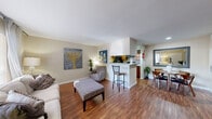 This thoughtfully designed one-bedroom, one-bathroom residence offers a practical and comfortable single-floor layout. Rich hardwood-style flooring flows throughout the main living areas, anchoring an open-concept space that seamlessly connects the living room, dining area, and kitchen.

The living room is bright and welcoming, featuring a large window that fills the room with natural light and provides a relaxed setting for everyday living. Adjacent to it, a compact yet functional dining nook offers just enough space for an intimate round table, complemented by a large wall mirror that enhances the sense of openness.

The kitchen is efficiently arranged with warm wood cabinetry, black appliances including a range and refrigerator, and a granite-topped breakfast bar that opens to the living area — ideal for casual dining or entertaining.

The bedroom is a generous, carpet-floored retreat featuring two windows, a ceiling fan, and ample space for a full furniture arrangement. The room offers a calm, restful ambiance with neutral tones throughout.

The bathroom is clean and functional, featuring a tiled tub-shower combination, a granite vanity countertop, and wood-style flooring. A hallway connects the rooms, completing this efficient and well-organized floor plan.