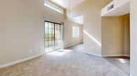 Located at 900 Country Club Dr SE in Rio Rancho, New Mexico, this single-floor, 2-bedroom, 2-bathroom residence offers a well-organized layout with a hallway, two closets, a utility room, and dedicated living and dining areas. The living room is a standout space, featuring soaring vaulted ceilings with a clerestory window that draws in abundant natural light. A ceiling fan adds comfort, while a sliding glass door provides direct outdoor access and views of surrounding greenery, creating an airy and open ambiance. Soft carpeting flows throughout the living and bedroom areas, complementing the warm, neutral-toned walls. The primary bedroom is generously proportioned with its own access to the hallway and a closet, while the secondary bedroom features a window with blinds that allows natural light to brighten the space. The combined dining and kitchen area is finished with light wood-style flooring and equipped with wood-accented cabinetry, black appliances including a range and refrigerator, and a built-in sink with a window above. Both bathrooms are cleanly appointed — one featuring a vanity with a granite-style countertop and mirrored wall, and the other a full tub-shower combination with tile-style flooring and a small window for ventilation.