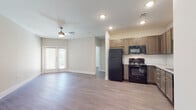 This single-floor residence offers a clean, modern design highlighted by consistent wood-look flooring and neutral tones throughout. The open-concept living area is bright and airy, featuring a ceiling fan and a set of French doors that fill the space with natural light and provide access to an outdoor patio. The kitchen is positioned adjacent to the living area and is well-equipped with a full suite of black appliances, including a refrigerator, electric range, built-in microwave, and dishwasher. Warm-toned, taupe cabinetry provides ample storage, while granite countertops and a classic white subway tile backsplash add refined detail. A stainless undermount sink completes the functional workspace. The bedrooms are comfortably sized, each with ceiling fans and windows dressed with horizontal blinds that allow for controlled natural light. Closet storage is included, with double doors in one bedroom. The bathroom features a glass-enclosed walk-in shower with white tile surround, a granite-topped vanity with a cabinetry base matching the kitchen, and a framed mirror. Throughout the unit, clean white baseboards and recessed lighting contribute to a polished, cohesive aesthetic. A wall-mounted thermostat is conveniently located near the main hallway.