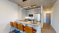Located in Chicago's vibrant Old Town neighborhood, this thoughtfully designed one-bedroom, one-bathroom residence offers a compelling blend of modern industrial aesthetics and contemporary comfort. Exposed concrete ceilings throughout lend an architectural edge to the bright, open interior, while light wood-tone flooring unifies the space seamlessly.

The open-concept kitchen and living area serves as the heart of the home. The kitchen features sleek two-tone cabinetry, stainless steel appliances, a subway tile backsplash, and a generous peninsula with quartz countertops and seating — ideal for casual dining or entertaining. Track lighting beneath the concrete ceiling adds a stylish, functional touch.

A light-filled hallway leads to the living room, which is anchored by expansive floor-to-ceiling windows that frame sweeping Chicago skyline views and flood the space with natural light.

The bedroom mirrors this connection to the outdoors with its own floor-to-ceiling window offering elevated city views, creating a bright and tranquil retreat.

The bathroom is finished with large-format neutral tiles, a walk-in glass-enclosed shower, and a dark-toned vanity with chrome fixtures, delivering a clean, spa-like feel. A dedicated closet completes this well-appointed residence.
