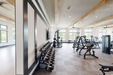 Located at 6735 Standifer Gap Rd in Chattanooga, TN, this expansive fitness center offers a comprehensive, single-floor layout designed to accommodate a wide range of workout needs. The facility is defined by its striking architectural character, featuring exposed natural wood beam ceilings that lend a warm, modern-rustic aesthetic throughout the space.

The main exercise area is generously sized, with plush carpet tile flooring and an extensive array of strength training equipment, including cable machines, weight racks stocked with dumbbells, multi-station cable systems, benches, and plate-loaded machines. Cardio equipment such as treadmills, ellipticals, and rowing machines are also well-represented. Large windows line the walls, flooding the space with natural light and offering views of the surrounding Chattanooga landscape. Full-length mirrors amplify the sense of space and allow for form monitoring during workouts.

A dedicated studio area features smooth hardwood flooring, floor-to-ceiling mirrors with bold navy accent stripes, and high ceilings — ideal for group fitness classes, stretching, or functional training. Ceiling fans throughout ensure comfortable air circulation. The overall ambiance is bright, clean, and professionally appointed, providing an inviting environment for a thorough fitness experience.