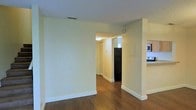 This two-floor residential space offers a clean and functional layout designed for comfortable everyday living. The interior is finished with warm hardwood floors that extend throughout the main living areas, creating a cohesive and inviting atmosphere. Neutral cream-toned walls and white baseboards contribute to a bright, airy feel that makes the space feel open and welcoming.

The main level features an open-concept flow between the living area and kitchen. The kitchen is equipped with essential appliances, including a refrigerator, microwave, and range, and is positioned adjacent to the main living area for convenient access. A hallway connects the living spaces, leading further into the home and providing a natural sense of depth and continuity.

Textured ceilings add a subtle architectural detail throughout, while ceiling-mounted light fixtures and HVAC vents indicate a well-integrated utility setup. The hallway at the rear of the main level receives natural light from a window, brightening the interior corridor.

Overall, the space presents a straightforward and practical design with consistent finishes across both floors, making it a functional and comfortable multi-level home.