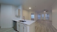 This well-appointed single-floor residence offers a clean, contemporary design throughout. The open-concept layout connects the kitchen directly to the living area, creating a seamless flow ideal for everyday living. The kitchen features white shaker-style cabinetry, a subway tile-patterned backsplash, stainless steel appliances including a refrigerator, electric range, and built-in microwave, as well as a peninsula with a double-basin sink — perfect for meal prep and casual dining. Light wood-style luxury vinyl flooring runs throughout the main living areas, lending a bright and airy feel. The spacious living room is filled with natural light from multiple windows and French doors that open to the outdoors, and is complemented by a ceiling fan overhead. The bedrooms are carpeted for added comfort, each offering generous proportions, ceiling fans, and ample closet space, including a walk-in closet in the primary suite. The primary bathroom is equipped with a dual-sink vanity, framed mirror, and a large soaking tub surrounded by marble-style tile. A dedicated in-unit laundry area adds everyday convenience. Throughout the space, white walls, recessed lighting, and consistent finishes create a cohesive, move-in-ready environment.