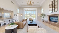Located at 12845 Frederick St in Moreno Valley, CA, this single-floor space seamlessly integrates a living room, dining area, and kitchen into a cohesive, open-concept layout. The most striking architectural feature is the dramatically soaring ceiling height, complemented by an expansive wall of floor-to-ceiling windows in the dining area that floods the space with natural light and offers sweeping views of a lush outdoor courtyard and pool area beyond. Warm-toned travertine tile flooring flows throughout, laid in an elegant diagonal pattern that enhances the sense of spaciousness. The living room is anchored by a stately fireplace with a classic decorative mantel and an oversized arched mirror above, adding depth and grandeur to the room. The kitchen is well-appointed with white raised-panel cabinetry, granite countertops, a coordinating tile backsplash, and stainless steel appliances, including a built-in microwave, electric cooktop, dishwasher, and refrigerator. A window above the sink brings in additional natural light. Throughout the space, crisp white walls and abundant natural light create a bright, airy ambiance, making this a welcoming and functional environment in the heart of Southern California.