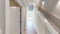 This two-story home in Springdale, Arkansas offers a well-designed layout with consistent modern finishes throughout. The main level features an open-concept living and kitchen area with light wood-look luxury vinyl plank flooring, neutral gray-toned walls, and ceiling fans. The kitchen is a standout feature, equipped with white shaker-style cabinetry, granite countertops, a full suite of stainless steel appliances including a refrigerator, electric range, and built-in microwave, and a central island with seating overhang. A half bathroom on the main level includes a granite-topped vanity and matching wood-look flooring.

The upper level is accessible via a bright hallway featuring recessed lighting and a skylight that brings in natural light. Bedrooms are carpeted and include ceiling fans, with the primary bedroom offering a walk-in closet with built-in shelving and rods, plus an additional standard closet. Additional rooms with carpet flooring provide flexible living space. The attached garage is spacious, equipped with an automatic opener, and provides interior access. Throughout the home, white panel doors and clean trim work contribute to a cohesive, contemporary aesthetic.