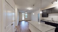 This single-floor residence offers a thoughtfully designed open-concept layout that seamlessly connects the kitchen and living areas. The kitchen is a standout feature, boasting dark espresso cabinetry that contrasts beautifully with light granite countertops, a matching granite-topped center island illuminated by stylish globe pendant lights, stainless steel appliances, and a track lighting system. Wood-look flooring runs throughout the main living areas, adding warmth and continuity to the space.

The living area is bright and welcoming, with a ceiling fan overhead, natural light streaming in through a glass-paneled front door with transom window, and direct sightlines to the kitchen island. The bedrooms feature plush carpeting, ceiling fans, and windows fitted with blinds for privacy and light control. One bedroom offers direct access to a private bathroom and walk-in closet equipped with built-in shelving, providing generous storage. The bathroom features dark cabinetry with granite countertops and a large mirror, consistent with the home's design language. An additional bedroom provides ample space and connects conveniently to the hallway. Clean white walls and neutral tones throughout create a bright, move-in-ready atmosphere.