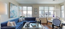 This contemporary single-floor residence offers a thoughtfully designed layout that balances modern style with everyday functionality. The kitchen is a standout space, featuring sleek white cabinetry, dark granite countertops, rich hardwood flooring, and a full suite of stainless steel appliances including a refrigerator, microwave, and range. A central island provides additional counter space and casual seating, making it ideal for both cooking and entertaining.

The living area is bright and inviting, anchored by large windows that frame sweeping panoramic city views. Natural light floods the room throughout the day, highlighting the warm hardwood floors and neutral-toned walls that complement the space's contemporary aesthetic.

The bedroom is a calm retreat finished with plush carpeting, warm neutral walls, and a well-sized window that continues to offer urban vistas. Soft, ambient lighting contributes to a restful atmosphere.

The bathroom is cleanly designed with white cabinetry, dark granite countertops, and a combination tub and shower finished in neutral tile. A large mirror above the vanity enhances the sense of space, while white tile flooring adds a crisp, clean finish. Overall, this residence presents a cohesive modern design with high-quality finishes throughout.