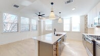 This single-floor residence showcases a clean, contemporary design defined by light hardwood flooring, crisp white walls, and an abundance of natural light streaming through multiple windows fitted with blinds. The open-concept kitchen serves as the centerpiece of the living area, anchored by a generously sized waterfall island with a sleek quartz countertop, an undermount stainless steel sink, and matte black fixtures. Pendant lighting with conical shades hangs above the island, complementing the modern aesthetic. The kitchen is well-appointed with light wood cabinetry, stainless steel appliances including a gas range, built-in microwave, and French door refrigerator, along with a classic white subway tile backsplash. Open shelving adds additional storage and display space nearby. The living area adjoins the kitchen seamlessly, complete with a ceiling fan and multiple windows that fill the space with natural light and outdoor views. The bedrooms are bright and well-proportioned, each featuring hardwood floors, ceiling fans, and windows offering exterior views. The bathroom is elegantly finished with large-format marble-style tile surrounding the soaking tub and shower, matte black hardware, a floating vanity with quartz countertop, neutral floor tile, and built-in open shelving for convenient storage.
