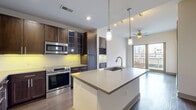 Located in the heart of Midtown Atlanta, this contemporary residence at 782 Peachtree St NE offers a thoughtfully designed open-concept layout with high-end finishes throughout. The gourmet kitchen serves as the focal point of the living space, showcasing rich dark wood cabinetry with glass-front accents, a built-in wine rack, stainless steel appliances including a range and built-in microwave, and a subway tile backsplash illuminated by under-cabinet lighting. A large central island with a sleek quartz countertop and an undermount sink provides generous prep space, while pendant lighting adds a refined touch overhead. Hardwood flooring flows through the main living and kitchen areas, complemented by a ceiling fan and large windows that frame views of the Atlanta skyline. The bedrooms feature plush carpeting, tray ceilings, and oversized windows that invite abundant natural light and city views. The bathroom is appointed with a bold blue vanity, quartz countertop, framed mirror, and large-format tile flooring. A spacious walk-in closet provides excellent storage. The residence also features a private balcony, offering a seamless connection to the vibrant Midtown Atlanta streetscape.