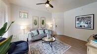This single-floor residence offers a thoughtfully designed layout with a cohesive, contemporary aesthetic. The living room is bright and inviting, featuring large windows dressed with wood-slat blinds that frame lush outdoor views, light wood-style flooring, and a ceiling fan overhead. The open sightlines to the adjacent dining area create a natural flow ideal for everyday living and entertaining.

The kitchen is sleek and functional, outfitted with white cabinetry, white quartz countertops, a dark tile subway backsplash, and a full suite of stainless steel appliances. Recessed lighting illuminates the well-organized galley-style layout efficiently.

The primary bedroom is generously proportioned, with a ceiling fan, sliding glass doors opening to an outdoor patio, and direct access to a spacious walk-in closet with built-in shelving. A secondary bedroom provides a comfortable and quiet retreat with neutral tones and framed wall art. Both bathrooms are finished with white vanities, quartz countertops, and light wood-style flooring — one featuring a shower-tub combination and the other a glass-enclosed shower.

Throughout the residence, light-toned walls, consistent flooring, and carefully selected fixtures contribute to a clean, modern ambiance that is both functional and visually cohesive.