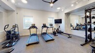 Located at 2110 Pickens St. in Columbia, SC, this fitness center is a thoughtfully designed, single-floor workout facility that combines functionality with a clean, modern aesthetic. The space is defined by crisp white walls, grey rubber flooring, and a combination of track lighting and ceiling-mounted fixtures that keep the environment well-lit throughout.

The cardio zone is generously outfitted with multiple TRUE treadmills, an elliptical trainer, a stationary air bike, and a rowing machine, providing a full range of cardiovascular training options. Natural light filters in through several windows adorned with decorative ironwork grilles, lending the space a bright and welcoming atmosphere. A wall-mounted flat-screen TV and a large ceiling fan add comfort for longer workout sessions.

A striking floor-to-ceiling glass partition with a bold black steel frame visually divides the fitness area from an adjacent hardwood-floored room, adding an architectural element that enhances the sense of openness. The strength training section is equipped with a full power rack with barbells and weight plates, a dumbbell rack with a comprehensive set of free weights, and an adjustable workout bench. A wall of mirrors further amplifies the sense of space and supports proper form during training. The overall design balances practicality with a polished, professional feel.