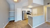 This single-floor residence offers a practical and comfortable layout designed for everyday living. The open-concept living and dining area greets you at the entry, featuring warm neutral-toned walls, plush carpeting, and vaulted ceilings that lend an airy sense of height. A tiled entryway transitions seamlessly into the living space, which extends toward a set of bright windows and a glass-paned door that invites natural light and provides outdoor access.

The kitchen is positioned adjacent to the living area and is equipped with stainless steel appliances, including a refrigerator and microwave, alongside a black range. White cabinetry offers ample storage, while a peninsula countertop creates a natural divide between the kitchen and living space, making it ideal for casual dining or meal prep. Wood-style flooring throughout the kitchen adds warmth and durability.

The bedrooms are carpeted and generously sized, each featuring neutral walls and windows that bring in natural light. The primary bedroom includes access to a walk-in closet with built-in shelving, offering substantial storage. Additional built-in shelving is found in other areas of the unit. The bathroom features a full tub-shower combo with white tile surround, a vanity with a countertop sink, and wood-style flooring.