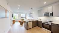 Located at 1700–1706 N Howard St in Philadelphia, PA, this well-appointed one-bedroom, one-bathroom unit offers a thoughtfully designed open-concept layout. Light wood flooring runs throughout, complementing crisp white walls and recessed lighting that keep the space feeling bright and contemporary.

The kitchen is a standout feature, equipped with stainless steel appliances including a French door refrigerator, electric range, built-in microwave, and dishwasher. Two-tone cabinetry pairs warm wood lower cabinets with muted grey uppers, topped with light quartz countertops. A peninsula with seating provides both additional prep space and a casual dining area. A sleek pendant light anchors the kitchen to the open living area, where large windows allow abundant natural light and views of the surrounding neighborhood.

The bedroom is a quiet, well-proportioned retreat with clean finishes and direct access to a dedicated closet featuring built-in shelving and hanging rods. The bathroom is finished in large-format grey tile, with a frameless glass walk-in shower, a floating vanity with a white countertop, and an illuminated mirror—creating a clean, spa-like feel. The overall design emphasizes modern minimalism with functional, high-quality finishes throughout.