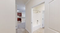 This single-floor residence offers a practical and comfortable layout across two bedrooms and two bathrooms. The kitchen is a standout feature, showcasing rich cherry wood cabinetry that extends to the ceiling, granite-style countertops, black appliances including a refrigerator, range, microwave, and dishwasher, and a peninsula with pendant lighting that opens toward the living area. The transition from tile flooring in the kitchen to plush carpet in the living and bedroom areas creates a clear distinction between spaces. The living room benefits from natural light through multiple windows, a ceiling fan, and direct access to an exterior door. The primary bedroom is generously sized with carpeted floors and direct access to one of the bathrooms. Both bathrooms are finished consistently with tile flooring, cherry wood vanities, granite-style countertops, and soaking tub and shower combinations. The second bedroom also features carpet flooring and access to a dedicated closet with built-in shelving. Crown molding throughout the common areas adds an architectural detail that elevates the overall finish of the space. The neutral color palette of warm beige tones throughout creates a cohesive and inviting ambiance.