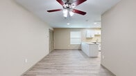 This single-floor unit offers a bright, open-concept layout that seamlessly connects the living area to the kitchen. Light wood-style vinyl flooring runs consistently throughout the space, creating a cohesive and clean aesthetic. The living area is equipped with a ceiling fan with integrated lighting and features a louvered bifold closet door, adding functional storage to the main living space.

The kitchen is well-appointed with crisp white shaker-style cabinetry, granite countertops, and a peninsula that provides additional prep and seating space. Black appliances — including a refrigerator, range, and dishwasher — offer a modern contrast to the white cabinetry. A window with blinds allows natural light to fill the kitchen.

The bedrooms continue the warm neutral palette with beige walls and the same light wood-style flooring. Each room includes a ceiling fan and benefits from natural light through windows fitted with blinds.

The bathroom is finished with large-format gray tile surrounding the tub and shower combination, complemented by a white vanity with granite countertops and chrome fixtures. The flooring mirrors the wood-style planks found throughout the rest of the unit, tying the design together cohesively. Overall, the space presents a clean, move-in-ready environment with consistent, contemporary finishes.