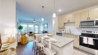 This single-floor residence features a thoughtfully designed open-concept layout that maximizes its footprint across four bedrooms and one full bathroom. The kitchen serves as a central highlight, showcasing light wood cabinetry with matte black hardware, a white subway tile backsplash, granite-style countertops, and a full suite of stainless steel appliances including a refrigerator, range, and microwave. A spacious island with seating for multiple guests flows naturally into the adjacent living area, which features wood-look flooring, a ceiling fan, and large windows with shutters that invite natural light. The living space provides access to an outdoor area via a glazed door. Each bedroom is finished with neutral tones, ceiling fans, and windows dressed with shutters and sheer curtains. The primary bedroom offers a comfortable, well-proportioned retreat with carpeted floors. The shared bathroom includes a granite-top vanity with a light wood base, a walk-in glass shower, and wood-look flooring. A dedicated laundry room houses a full-size washer and dryer with overhead shelving, adding practical convenience throughout.