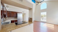 Located at 2901 Euclid Ave NE in Albuquerque, New Mexico, this two-bedroom, two-bathroom unit offers a well-designed single-floor layout that maximizes functionality and comfort. The open living room is a standout, boasting dramatic vaulted ceilings with a striking arched clerestory window alongside a full-length window that floods the space with natural light and views of the surrounding neighborhood. Warm hardwood-style flooring runs throughout the entire unit, creating a cohesive and inviting atmosphere.

The kitchen is well-appointed with rich dark wood cabinetry, granite countertops, a tile backsplash, and a full suite of stainless steel appliances including a refrigerator, range, dishwasher, and built-in cooktop. A peninsula with a granite overhang connects the kitchen to the living area, offering a casual dining or entertaining space.

The spacious primary bedroom features a sliding glass door opening to a private balcony with outdoor views, while the second bedroom enjoys a large window overlooking mature trees. Two hallways connect the private areas of the unit efficiently. The first bathroom includes a tiled tub-shower combination, while the second features a glass-enclosed shower and a dark-stained vanity with a white basin sink. Track and pendant lighting add polished finishing touches throughout.