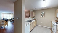 Located at 1070 Kenmore Dr in Clayton, NC, this single-floor residence offers a well-organized layout with a warm, cohesive aesthetic throughout. The living room serves as the heart of the home, featuring durable wood-look flooring, soft neutral walls, and a generous window that fills the space with natural light and offers views of the surrounding greenery. The open-concept dining area connects seamlessly to the kitchen via a pass-through counter, making it ideal for everyday living. A pendant light anchors the dining space, which flows naturally from the living area. The galley-style kitchen is thoughtfully designed with light wood cabinetry, a double-basin sink, a full suite of white appliances including a dishwasher, range, and refrigerator, and ample counter space along both sides. The bedroom is a restful retreat with plush carpeting, a ceiling fan, and a large window that invites natural light while providing outdoor views. The bathroom is clean and functional, finished with wood-look flooring and a shower-tub combination. Throughout the residence, a consistent palette of soft greiges and warm neutrals creates a calm, inviting atmosphere.