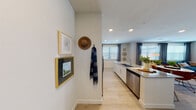 This single-floor residence features a thoughtfully designed open-concept layout that seamlessly connects the kitchen, dining, and living areas. The kitchen is well-appointed with white shaker cabinetry extending to the ceiling, granite countertops, a large center island with an integrated sink, and a full suite of stainless steel appliances including a side-by-side refrigerator, range, microwave, and dishwasher. Recessed lighting illuminates the space, while a window allows natural light to fill the room.

The open living and dining area is bright and spacious, benefiting from multiple large windows dressed with blinds and drape panels that invite generous natural light. A ceiling fan provides comfort throughout the space, and light-toned hardwood-style flooring runs consistently across the entire unit, enhancing the sense of flow and continuity.

The bedroom is a comfortable retreat featuring a ceiling fan, a well-sized window with natural light, and ample room for furnishings. The bathroom connects directly to a walk-in closet equipped with built-in shelving and hanging rods, offering practical storage. The entry hallway provides a welcoming transition into the home, complete with wall hooks and a clean, neutral palette that defines the overall modern and cohesive aesthetic of the space.