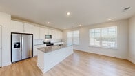 Located at 1010 Rosefinch Landing in Hoschton, Georgia, this single-story home offers a bright and modern interior defined by clean lines and a crisp, neutral color palette. The open-concept kitchen serves as the heart of the home, showcasing tall white shaker cabinets, granite countertops, a large central island with an integrated sink, and a full suite of stainless steel appliances including a refrigerator with ice maker, microwave, and range. Light hardwood-style flooring flows throughout the main living and kitchen areas, complementing the abundant natural light that pours in through oversized windows fitted with blinds. An adjacent room with multiple large windows provides additional flexible living or dining space. The bedrooms are carpeted for comfort, with one spacious primary bedroom featuring a ceiling fan and generous natural light. A dedicated walk-in closet offers extensive wire shelving along both walls, providing substantial storage. A well-appointed hallway connects the bedrooms to a full bathroom complete with a tub-shower combo, granite vanity top, and hardwood-style flooring. A laundry area is conveniently located along the interior hallway, rounding out this well-designed, move-in-ready home.
