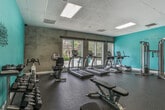 Located at 1049 Powers Ferry Rd SE in Marietta, Georgia, this fitness center is a single-floor facility designed to support a comprehensive workout experience. The space is defined by its vibrant teal accent walls, durable rubber flooring, and a drop-panel ceiling fitted with recessed fluorescent lighting that ensures a bright, well-lit environment throughout.

The cardio zone is positioned along a wall of large, multi-pane windows that frame views of an outdoor pool and mature tree canopy, offering a refreshing backdrop during workouts. This area houses multiple treadmills and elliptical cross-trainers from True Fitness, providing ample options for aerobic exercise.

The strength training section is well-appointed with a cable cross-over machine, multiple selectorized weight machines for targeted muscle training, a flat workout bench, and a rack stocked with a graduated set of dumbbells. Full-length wall mirrors span a significant portion of the room, enhancing the sense of openness and allowing users to monitor their form.

A motivational "Fitness" wall decal adds a purposeful touch to the space. The overall layout is open and thoughtfully organized, allowing for comfortable circulation between equipment zones. The combination of natural light, modern equipment, and functional design makes this fitness center a practical and inviting amenity.