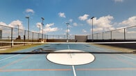 Located at 215 N Pine Street in the heart of Charlotte, NC, this rooftop sports facility offers a dynamic, open-air recreational experience elevated above the city. The centerpiece of the space is a multi-use court finished in a vibrant blue surface, thoughtfully lined for both tennis and basketball play. A regulation tennis net bisects the court for tennis use, while a freestanding adjustable basketball hoop provides a second sporting option — making the space highly versatile for residents and guests alike.

The court is enclosed by a sturdy chain-link perimeter fence, ensuring safety while preserving open sightlines to the surrounding Charlotte skyline. Multiple high-mounted stadium-style light poles ring the court, enabling use well into the evening hours. The "Charlotte" branding emblazoned at center court reinforces the local identity of the space.

Adjacent to the court, a landscaped lounge area features raised planter beds with tropical palm trees, seating arrangements, and decorative greenery, offering a relaxing retreat between games. The surrounding urban backdrop, including the modern glass-and-balcony residential tower rising directly alongside the court, adds a striking architectural contrast to the open sky above. With sweeping views of the Charlotte cityscape and an abundance of natural light, this rooftop court delivers both athletic functionality and a premium urban outdoor atmosphere.