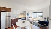 Located at 1061 NE Ninth Ave in Portland, Oregon, this well-appointed one-bedroom residence offers a smart, efficient layout across a single floor. The welcoming entrance leads into a bright, open-concept living, dining, and kitchen area bathed in natural light. Large windows frame sweeping views of the Portland skyline and surrounding cityscape, creating a compelling backdrop for everyday living.

The kitchen is outfitted with two-tone cabinetry — rich walnut-finish lower cabinets paired with crisp white upper cabinets — along with stainless steel appliances including a full-size refrigerator, range, and built-in microwave. Light-toned countertops and warm hardwood-style flooring complete the space. The adjacent dining area accommodates a full table and opens seamlessly into the living room, which benefits from generous window light and elevated city views.

The bedroom features plush carpeting, large windows with the same impressive outlook, direct access to a bathroom, and a dedicated closet. Two full bathrooms serve the residence, each featuring clean white tile and tub-shower combinations. An in-unit laundry area and two closets provide practical storage throughout. The overall aesthetic is modern and clean, with a neutral palette that creates a calm, cohesive ambiance throughout.