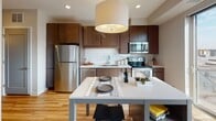 Located at 1300 W Lake St in Minneapolis, MN, this contemporary single-floor unit offers a thoughtfully designed open-concept layout with modern finishes throughout. The entryway features light wood-style flooring that flows seamlessly into the main living areas, with a stylish sliding glass-panel door providing access to the bedroom, adding a sleek, space-conscious touch.

The living area is a standout, anchored by expansive floor-to-ceiling sliding glass doors that frame sweeping views of the Minneapolis skyline and surrounding neighborhood, flooding the space with abundant natural light. The open kitchen is well-equipped with rich dark wood cabinetry, stainless steel appliances including a refrigerator, range, and over-the-range microwave, complemented by white subway tile backsplash and light stone countertops. A kitchen island with bar seating doubles as a dining area, making the space ideal for both everyday living and entertaining.

The bedroom, accessed via the modern sliding door, offers a quiet retreat with carpeted flooring. The bathroom is clean and contemporary, featuring large-format dark tile flooring, a full soaking tub with tiled surround, a floating wood vanity with a white countertop, and crisp white walls that lend a calm, spa-like ambiance.