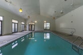 This indoor pool facility at 8064 S Fulton Pkwy in Fairburn, Georgia, offers a well-appointed aquatic space designed for year-round use. The centerpiece of the facility is a generously sized indoor swimming pool with clear turquoise water, accessible via stainless steel entry rails. The pool is surrounded by a wide concrete pool deck, providing ample space for movement and safety.

The architecture features soaring vaulted ceilings accented by pendant light fixtures and ceiling fans, creating an airy and open atmosphere. A series of large, multi-pane French doors line the walls, flooding the interior with natural light and offering views of the lush green landscaping and grounds outside. These doors also provide convenient access points to the exterior of the facility.

The entry area of the facility displays prominently posted pool rules and safety notices, reflecting a well-managed and safety-conscious environment. Tile wainscoting along the lower walls adds a clean, finished aesthetic throughout the space. The facility is equipped with standard safety equipment, including a fire extinguisher and emergency exit signage, ensuring compliance with safety standards.

Overall, the space presents a bright, functional, and welcoming indoor aquatic environment, well-suited for both recreational swimming and structured aquatic programs.