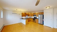 Located at 237 North Ave, Unit 21 in Burlington, Vermont, this two-bedroom, one-bathroom unit offers a functional and well-appointed single-floor layout. The open-concept kitchen and living area is anchored by a peninsula with dark countertops, warm honey-toned cabinetry, and a full suite of stainless steel appliances including a gas range, built-in microwave, and refrigerator. Recessed lighting and a ceiling fan complement the light hardwood-style flooring that flows throughout the main living space. A wall-mounted mini-split unit provides efficient climate control in both the kitchen/living area and the primary bedroom. A bright, carpeted hallway connects the living area to both bedrooms, a full bathroom, and a closet. Each bedroom features plush carpeting, a ceiling fan, and baseboard heating. The primary bedroom includes a wall-mounted mini-split and a window with outdoor views, while the second bedroom also enjoys natural light through its window. The full bathroom is clean and straightforward, offering a tub/shower combo, toilet, and a wood-vanity with a single sink. The layout is practical and efficient, making good use of the available space throughout.