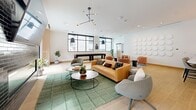 Located at 955 Bannock St in Denver, CO, this rooftop lounge is a thoughtfully designed communal space that blends modern aesthetics with functional amenities. The open-plan layout seamlessly connects a fully equipped kitchen with a spacious living and entertainment area, all finished with warm light hardwood flooring throughout.

The kitchen features floor-to-ceiling wood cabinetry in a natural oak tone, a textured stone backsplash, stainless steel appliances, and a generous waterfall-edge island with seating for multiple guests. A sculptural multi-pendant light fixture anchors the space above the island, adding a striking design element.

The living area is generously proportioned and bathed in natural light from large black-framed windows. It is furnished with a tufted caramel leather sofa, contemporary accent chairs, and a full-length shuffleboard table, making it ideal for social gatherings. A decorative wall installation of circular white panels adds an artistic focal point.

A separate lounge alcove features a dark tile fireplace and large sliding glass doors that open directly onto an outdoor terrace, where additional seating and urban views of Denver create an inviting extension of the interior. The overall ambiance is clean, contemporary, and energetic — well-suited for community events and social entertainment.