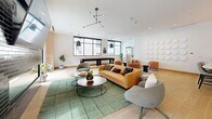 Located at 955 Bannock St in Denver, CO, this rooftop lounge is a thoughtfully designed communal space that blends modern aesthetics with functional amenities. The open-plan layout seamlessly connects a fully equipped kitchen with a spacious living and entertainment area, all finished with warm light hardwood flooring throughout.

The kitchen features floor-to-ceiling wood cabinetry in a natural oak tone, a textured stone backsplash, stainless steel appliances, and a generous waterfall-edge island with seating for multiple guests. A sculptural multi-pendant light fixture anchors the space above the island, adding a striking design element.

The living area is generously proportioned and bathed in natural light from large black-framed windows. It is furnished with a tufted caramel leather sofa, contemporary accent chairs, and a full-length shuffleboard table, making it ideal for social gatherings. A decorative wall installation of circular white panels adds an artistic focal point.

A separate lounge alcove features a dark tile fireplace and large sliding glass doors that open directly onto an outdoor terrace, where additional seating and urban views of Denver create an inviting extension of the interior. The overall ambiance is clean, contemporary, and energetic — well-suited for community events and social entertainment.