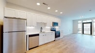 Located at 300 E Fifth Ave in Columbus, Ohio, this single-floor unit offers a thoughtfully designed layout with modern finishes throughout. Light hardwood flooring runs continuously across the living, kitchen, and bathroom areas, creating a cohesive and airy feel.

The kitchen is a standout feature, boasting full-height white shaker cabinetry that maximizes storage, a classic white subway tile backsplash, and crisp quartz countertops. A complete suite of stainless steel appliances — including a refrigerator, electric range, built-in microwave, and dishwasher — provides a fully equipped cooking environment. A matte black faucet at the undermount sink adds a contemporary contrast to the bright, clean palette. Recessed lighting illuminates the space efficiently overhead.

The living area is open and bright, benefiting from large windows with floor-to-ceiling black-framed glass that invite natural light and offer views of the surrounding streetscape. The open-concept flow between the kitchen and living space enhances the overall sense of roominess.

The bathroom maintains the same modern aesthetic, featuring a white shaker vanity with a clean countertop, a framed rectangular mirror, matte black hardware and fixtures, and consistent hardwood-style flooring. The space is clean, functional, and well-appointed throughout.