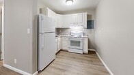 This well-organized single-floor unit offers a practical and functional layout across its four rooms: a bedroom, kitchen, bathroom, and closet. The interior is finished with warm-toned vinyl plank flooring throughout the main living areas, complemented by neutral gray walls and crisp white baseboards, creating a clean, cohesive look.

The spacious bedroom features painted concrete block walls with a window fitted with blinds, allowing for natural light while maintaining privacy. The room provides a comfortable footprint, accommodating standard furnishings with ease.

The kitchen is efficiently laid out in an L-shape, featuring white cabinetry, light granite-style countertops, and white appliances including a refrigerator and an electric range with overhead ventilation. The flooring continues the wood-look vinyl plank theme, and a flush-mount ceiling light keeps the space bright and functional.

The bathroom is finished with large-format marble-look tile flooring and an all-white design, including a full tub and shower unit with brushed nickel fixtures, a toilet, and a vanity with under-sink storage. White panel doors and clean trim complete the polished look.

Overall, this unit presents a neat, move-in-ready space with consistent finishes, efficient use of its footprint, and a neutral palette suitable for a variety of décor styles.