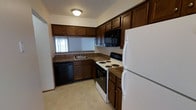 This multi-story residence spans three floors, offering a versatile and functional layout suited for comfortable everyday living. The kitchen is a highlight of the home, designed with efficiency in mind. Rich, dark-stained wood cabinetry lines the walls, providing generous storage space above and below the countertops. The kitchen is equipped with a full suite of appliances, including a white refrigerator, an electric coil range with oven, a built-in black microwave, and a dishwasher — everything needed for convenient meal preparation. Dark laminate countertops complement the cabinetry, and a single-basin sink is positioned beneath a window, allowing natural light to brighten the workspace. The light-toned flooring adds a clean contrast to the darker tones throughout the kitchen. The three-floor layout of the residence provides a natural separation of living spaces, offering distinct areas for common activities, rest, and additional uses. Each level contributes to an organized flow throughout the home. Overall, the space presents a practical and well-appointed interior with classic finishes that create a warm, functional environment suited to daily life.