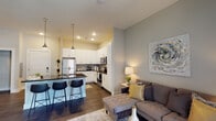 Located in Jacksonville, FL (32207), this thoughtfully designed single-floor residence combines modern aesthetics with functional living. The open-concept layout seamlessly connects the kitchen, dining, and living areas, creating a bright and cohesive space. Dark hardwood-style flooring flows consistently throughout, providing a warm contrast to the neutral gray and white color palette on the walls.

The kitchen is a standout feature, equipped with stainless steel appliances including a refrigerator, range, and microwave. Crisp white cabinetry extends to the ceiling for ample storage, complemented by dark granite countertops and a subway tile backsplash. A kitchen island with seating offers additional workspace and casual dining.

The living area is bathed in natural light from tall French doors that open to an outdoor balcony, with transom windows above adding further brightness. The bedroom offers a comfortable retreat with a large window providing outdoor views, elevated ceilings, and direct access to a walk-in closet.

The bathroom features white cabinetry, a granite-topped vanity with a wide framed mirror, and a full tub-shower combination. The entryway provides a welcoming introduction to the space, accented by decorative wall planters. Overall, the residence offers a clean, contemporary ambiance suited for modern living.
