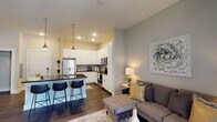 Located in Jacksonville, FL (32207), this thoughtfully designed single-floor residence combines modern aesthetics with functional living. The open-concept layout seamlessly connects the kitchen, dining, and living areas, creating a bright and cohesive space. Dark hardwood-style flooring flows consistently throughout, providing a warm contrast to the neutral gray and white color palette on the walls.

The kitchen is a standout feature, equipped with stainless steel appliances including a refrigerator, range, and microwave. Crisp white cabinetry extends to the ceiling for ample storage, complemented by dark granite countertops and a subway tile backsplash. A kitchen island with seating offers additional workspace and casual dining.

The living area is bathed in natural light from tall French doors that open to an outdoor balcony, with transom windows above adding further brightness. The bedroom offers a comfortable retreat with a large window providing outdoor views, elevated ceilings, and direct access to a walk-in closet.

The bathroom features white cabinetry, a granite-topped vanity with a wide framed mirror, and a full tub-shower combination. The entryway provides a welcoming introduction to the space, accented by decorative wall planters. Overall, the residence offers a clean, contemporary ambiance suited for modern living.