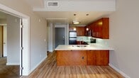This well-appointed single-floor residence offers a thoughtfully designed layout with a seamless blend of modern finishes and functional living spaces. The open-concept kitchen serves as the heart of the home, showcasing rich warm-toned wood cabinetry, white quartz countertops, and a glass tile backsplash. A peninsula with a double stainless steel sink extends into the living area, ideal for casual dining or entertaining. Stainless steel appliances, including a refrigerator, range, and over-the-range microwave, complete the kitchen's polished look. Pendant lighting above the peninsula adds a stylish focal point. Light hardwood flooring flows throughout the main living areas, creating a bright and cohesive feel, while large windows invite natural light into the living space. The bedroom areas feature plush carpeting and neutral warm-toned walls, offering a comfortable retreat. A window in the bedroom provides additional natural light. The bathroom includes a dark wood vanity with white countertop, a framed mirror, and wall-mounted lighting, maintaining the consistent modern aesthetic found throughout the space. Clean lines, neutral tones, and quality finishes define the overall ambiance of this residence.
