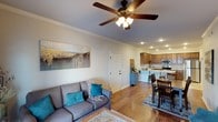 This 2-bedroom, 2-bathroom single-story home offers a thoughtfully designed open-concept layout that maximizes functionality and flow. The living area features warm hardwood flooring, crown molding, and a ceiling fan with integrated lighting, creating a comfortable and inviting atmosphere. Recessed lighting throughout adds a modern touch while ensuring the space is well-lit. A large decorative wall canvas adds a pop of artistic character to the living room.

The living space transitions seamlessly into a dedicated dining area, complete with a classic wooden dining set, before opening into the kitchen. The kitchen is equipped with stainless steel appliances, including a microwave and range, and features rich wooden cabinetry that provides ample storage. A breakfast bar with seating offers a convenient casual dining option and serves as a natural divider between the kitchen and living spaces.

The overall design aesthetic is warm and cohesive, with neutral wall tones complemented by natural wood accents throughout. Crown molding adds a refined architectural detail that elevates the interior. The open floor plan promotes easy movement between rooms, making the home feel spacious and welcoming — ideal for both everyday living and entertaining.