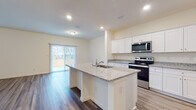 This two-story home is designed with a clean, modern aesthetic and a thoughtful layout that balances open communal spaces with private retreats. The main level centers around an expansive open-concept living and kitchen area, where light wood-look flooring flows seamlessly throughout. The kitchen is a functional showpiece, featuring crisp white cabinetry, granite countertops, a large center island with a built-in sink, and a full suite of stainless steel appliances including an electric range, microwave, and refrigerator. A walk-in pantry provides generous storage, while recessed lighting brightens the entire space. Sliding glass doors in the living area open to the outdoors, inviting natural light and outdoor views. A convenient half bath with a pedestal sink is also located on the main level. Upstairs, the bedrooms offer a quieter retreat, carpeted for comfort and sized generously for flexible use. The upper-level full bathroom features a glass-enclosed shower, a wide white vanity with ample counter space, and wood-look tile flooring. A dedicated laundry room with washer and dryer hookups adds everyday convenience, while a spacious walk-in closet with dual hanging rods offers excellent storage. The home presents a fresh, move-in-ready environment throughout.