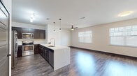 This two-story residence is designed with a modern, open-concept layout that seamlessly connects the kitchen and living areas. The kitchen is a standout feature, equipped with a full suite of stainless steel appliances, including a French door refrigerator, electric range, and built-in microwave. Rich, dark espresso cabinetry extends to the ceiling, offering generous storage, while light quartz countertops provide a striking contrast. A large kitchen island with an undermount sink and pendant lighting above serves as both a functional workspace and a natural gathering point.

The open living area extends from the kitchen, finished with dark hardwood-style flooring that runs throughout the main level. A ceiling fan with a light fixture keeps the space comfortable, and multiple windows with horizontal blinds allow natural light to fill the room.

A dedicated laundry room houses a full-sized washer and dryer set with overhead wire shelving for added storage convenience. The bathroom features a tiled tub-shower combination, a dark vanity with a quartz countertop, and hardwood-style flooring.

A carpeted staircase with a wall-mounted handrail connects the two floors. The attached garage provides secure parking and houses a water heater, with overhead fluorescent lighting and an automatic opener.