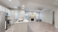 This single-floor residence offers a thoughtfully designed open-concept layout that maximizes its comfortable footprint across eight distinct spaces. The living area serves as the heart of the home, highlighted by a classic white-mantled fireplace flanked by two arched windows that flood the room with natural light. Crown molding, a ceiling fan, and a textured ceiling add refined detail to the space.

The kitchen flows seamlessly into the living area and features a peninsula with a built-in sink and white quartz countertops, white cabinetry, and stainless steel appliances, including a gas range and microwave. Recessed lighting overhead keeps the space bright and functional.

A separate room with French doors and transom windows offers flexible use as a dining area or den, while additional bedrooms provide comfortable, well-lit retreats. One standout bedroom features a tray ceiling with a central recessed light, lending an architectural elegance to the room. All bedrooms are finished with light wood-look flooring and ceiling fans with crown molding accents.

The bathrooms are outfitted with white shaker-style cabinetry, light countertops, framed mirrors, and tub-shower combinations. Light wood-look flooring runs consistently throughout the entire residence, tying each space together with a clean, cohesive aesthetic.