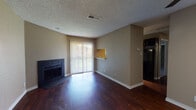 This single-floor residence offers a well-organized layout that balances comfort and functionality throughout its living spaces. The living room serves as the central gathering area, highlighted by a striking dark-tiled fireplace and rich hardwood-style flooring that runs throughout the main areas. A sliding glass door floods the room with natural light and provides outdoor access, while a pass-through counter connects seamlessly to the adjacent kitchen area. The galley-style kitchen is outfitted with dark cabinetry, light granite-style countertops, a stainless steel sink, track lighting, and black appliances including a full-size refrigerator, creating a sleek and cohesive aesthetic. The bedrooms feature warm, neutral-toned walls and plush carpeting, offering a comfortable retreat. One bedroom includes a built-in closet with shelving, while another benefits from a window with views of surrounding greenery. The bathroom is well-appointed with dark wood cabinetry, granite-style countertops, wood-look flooring, and accessibility grab bars, reflecting thoughtful design. Textured ceilings are consistent throughout the space, and a ceiling fan in the bedroom adds both style and practicality. Overall, the space presents a cohesive, neutral palette with durable finishes suited for everyday living.
