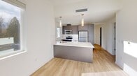Located in Federal Way, WA, this two-bedroom, one-bathroom unit offers a thoughtfully designed layout with modern finishes. Light wood-look flooring runs throughout the space, complementing the crisp white walls and creating a clean, contemporary aesthetic.

The open-concept kitchen serves as a central feature, equipped with stainless steel appliances including a refrigerator, range, and microwave, dark taupe cabinetry, and a white quartz peninsula with pendant lighting above. A subway tile backsplash and an under-mount sink add functional style, while a window brings in natural light and views of surrounding greenery.

A welcoming hallway connects the main living areas to the two bedrooms, each featuring light-filled windows — one with views of neighboring architecture and another with a serene natural wooded backdrop. The primary bedroom offers a comfortable footprint suited for a full bedroom suite. Both rooms share clean white walls and consistent flooring.

The bathroom features a backlit vanity mirror, dark wood cabinetry with a white countertop, and light wood flooring, creating a modern and well-appointed space. A dedicated utility room adds practical storage and functionality. The overall ambiance is bright, minimal, and move-in ready.